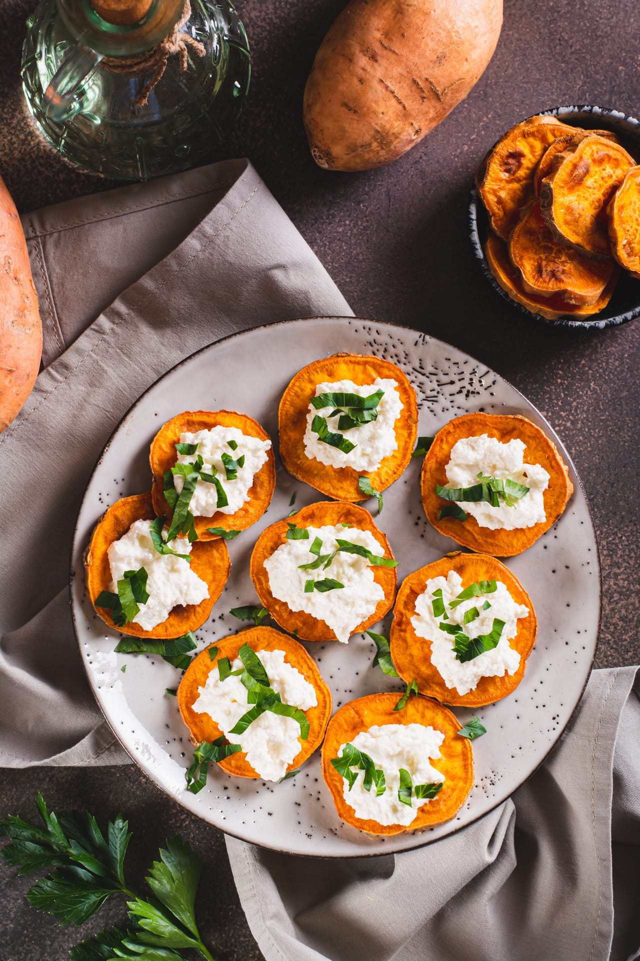 Roasted sweet potato rounds topped with soft white cheese and ribbons of fresh basil on a speckled grey plate